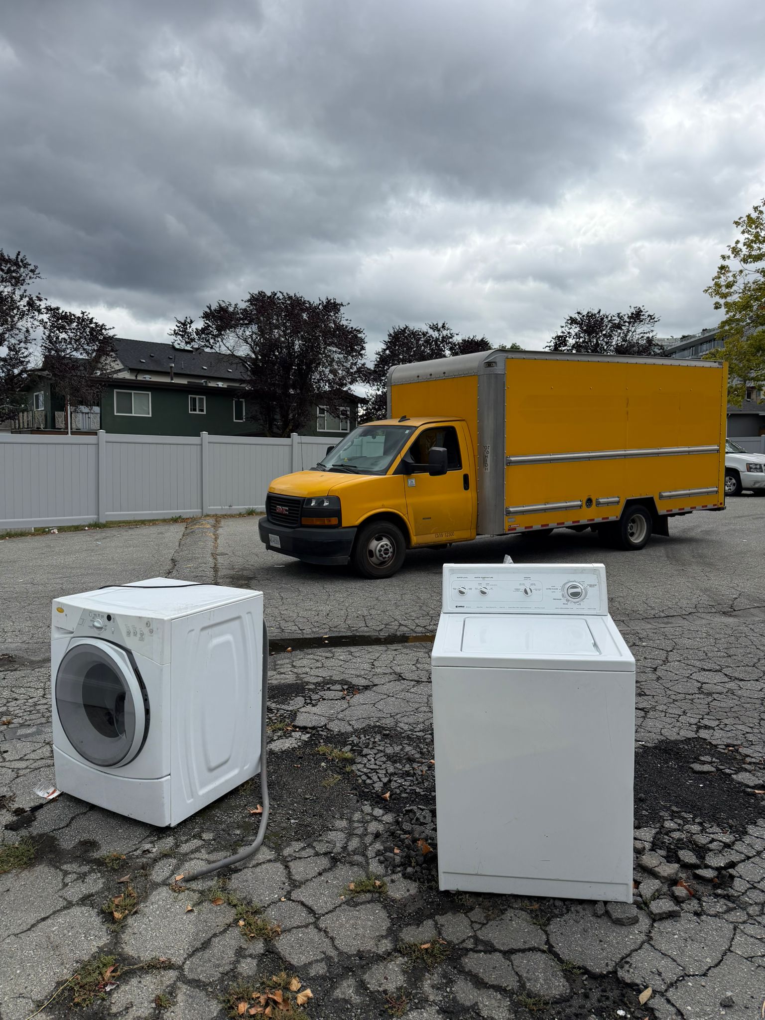 Junk Removal Express yellow box truck on a same-day appliance pickup in Surrey, BC, with a washer and dryer curbside ready to be hauled away