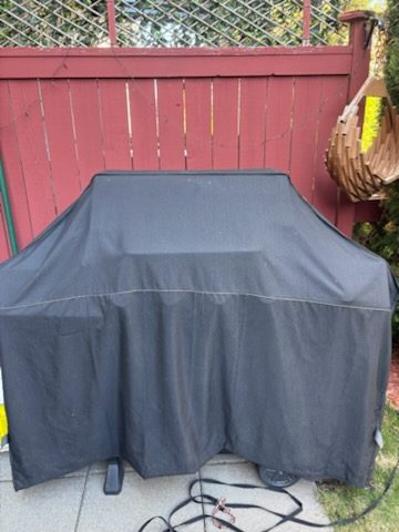 Gas barbecue under a grey cover on a patio, ready for barbecue removal