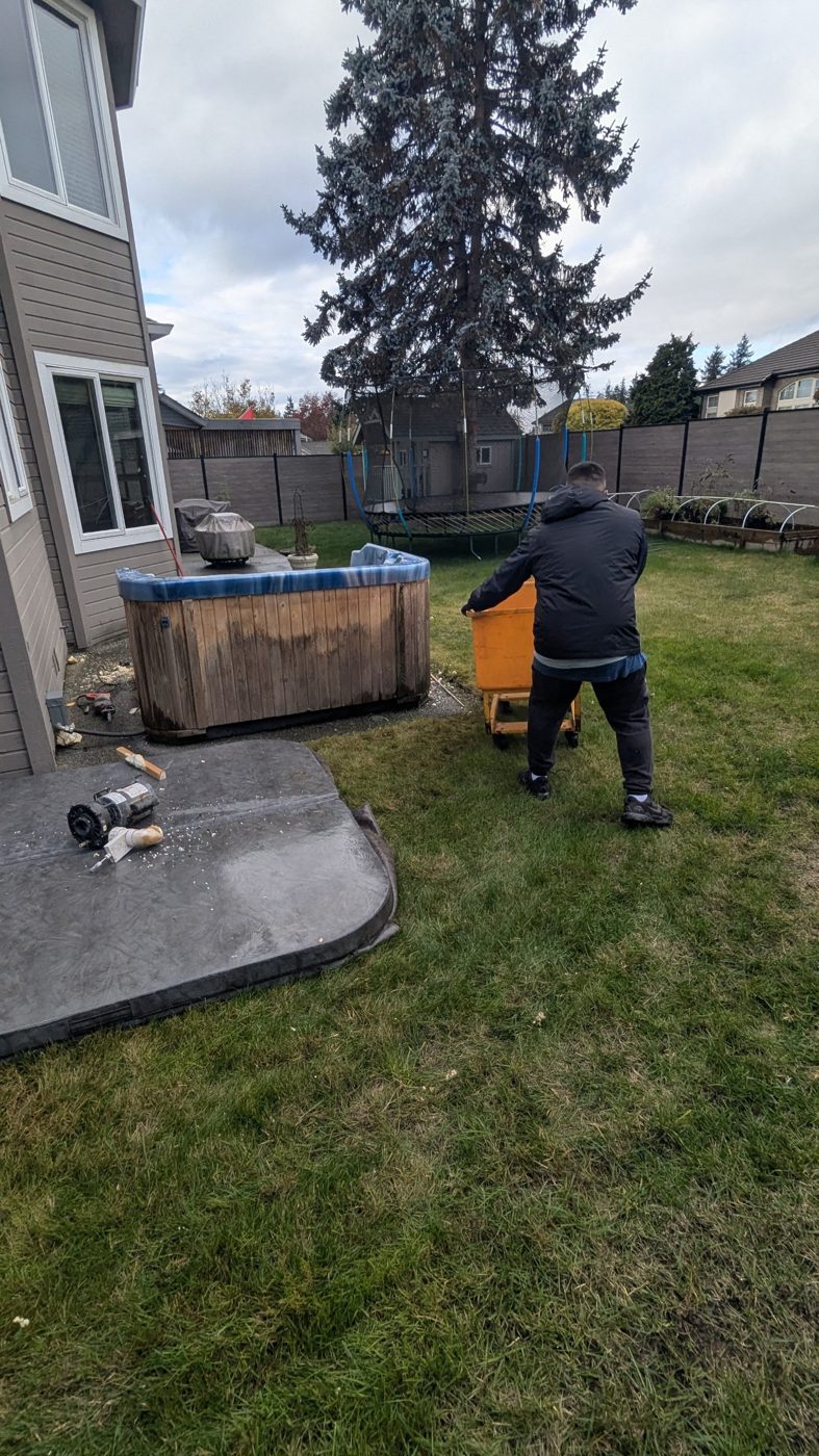 Junk Removal Express crew member wheeling an orange bin next to a backyard hot tub during hot tub removal