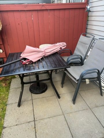 Black metal patio table with two grey chairs and a folded umbrella ready for patio furniture removal